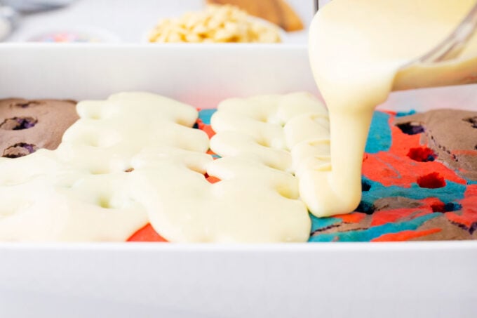 Pouring white chocolate mixture over unicorn poke cake.