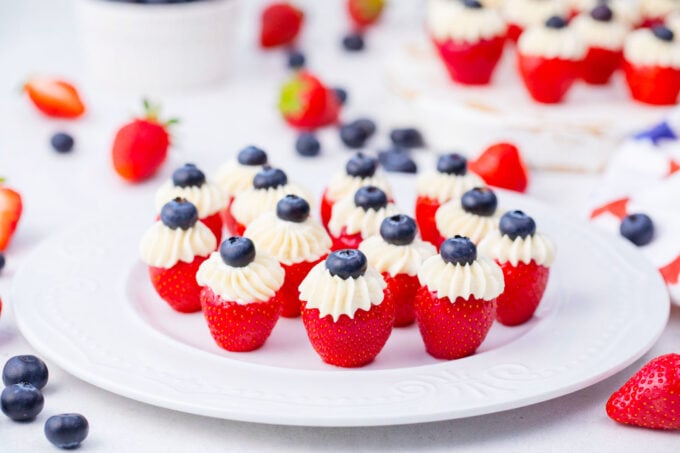 Red, white, and blue cheesecake stuffed strawberries with blueberries on a serving plate.
