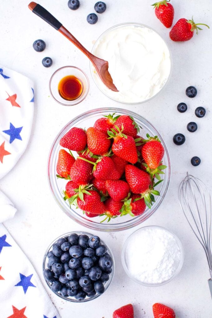Overhead shot of patriotic stuffed strawberries ingredients in bowls on a table.