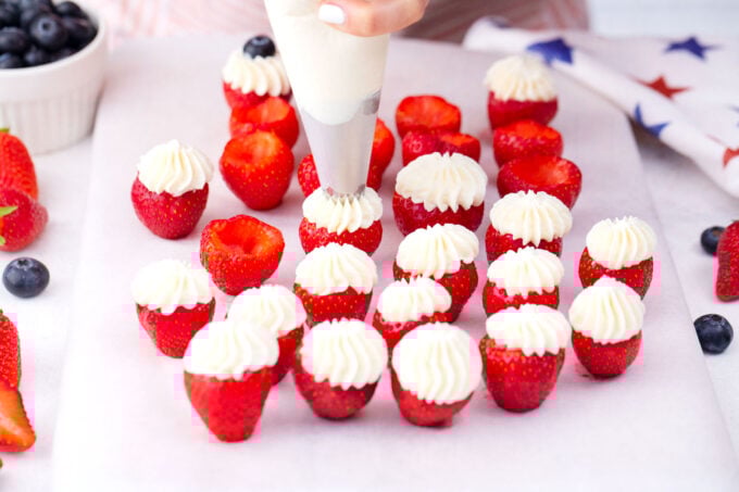 Piping cheesecake mixture into hulled strawberries.