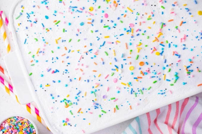 Overhead shot of unicorn poke cake topped with whipped cream and sprinkles.