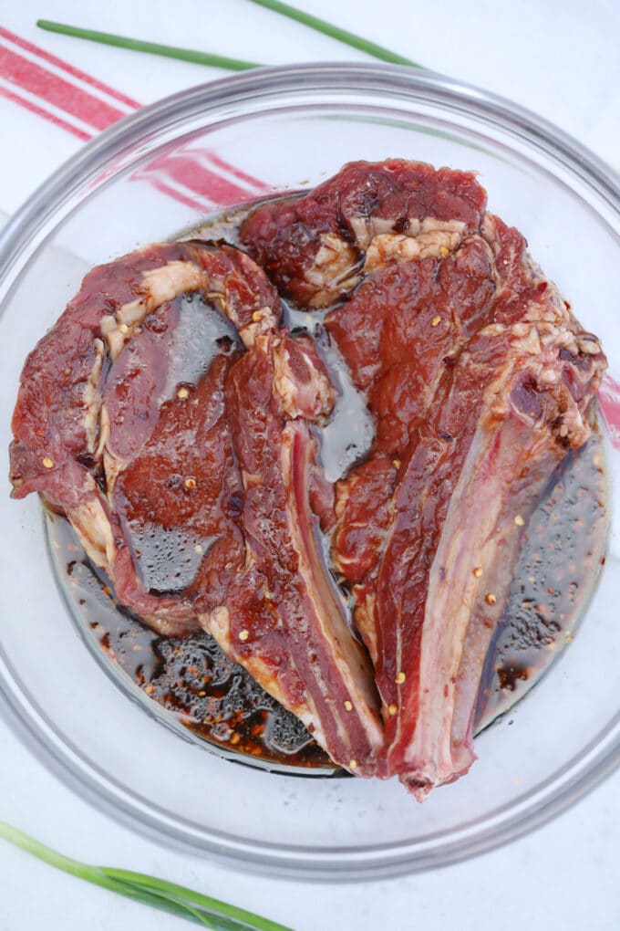 ribeye steaks in Asian steak marinade in a bowl.