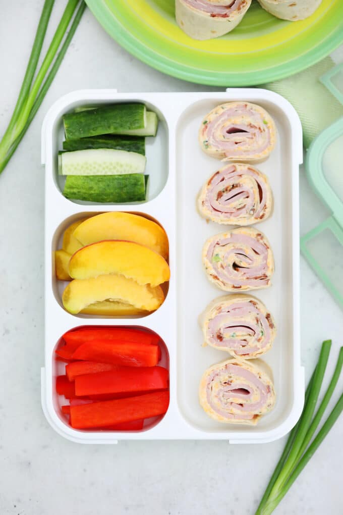 Picture of turkey pinwheels in with sliced cucumber and red bell peppers in a lunch box.