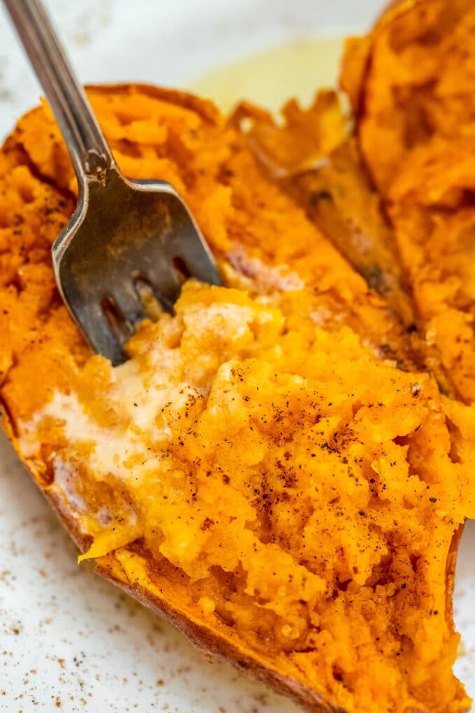 Forked sweet potato garnished with butter and cinnamon.