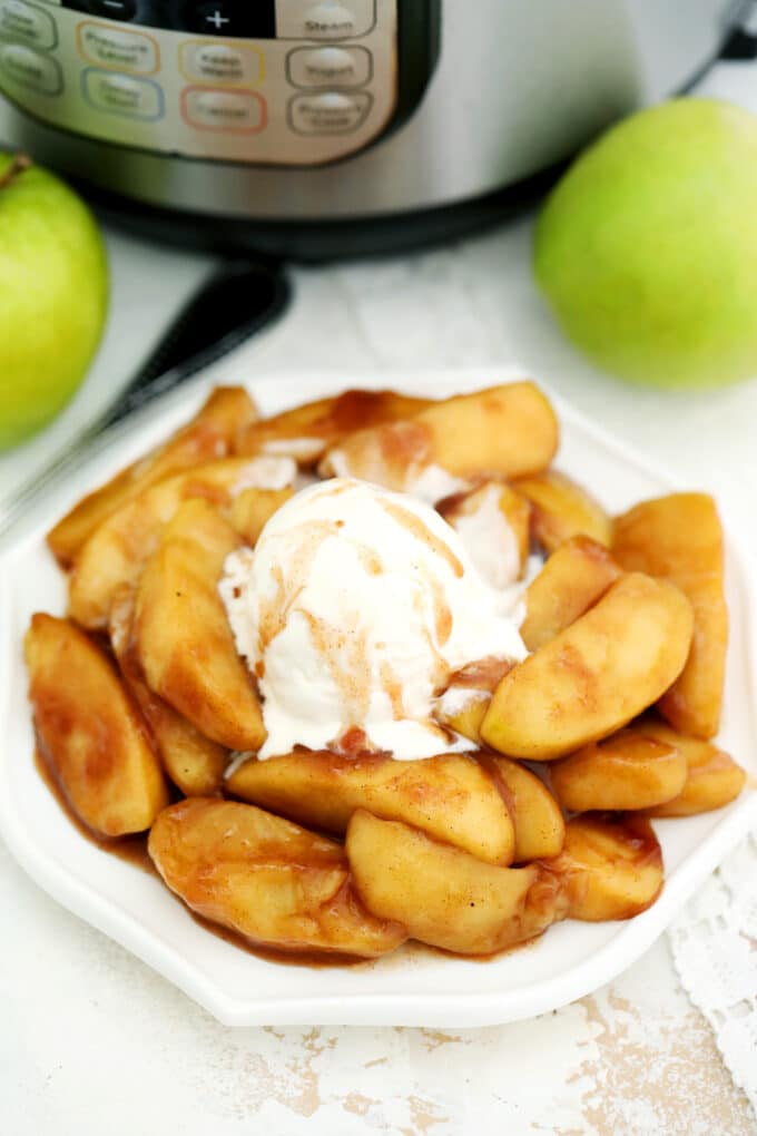 Image of cooked cinnamon apples topped with ice cream and caramel on a white plate. 