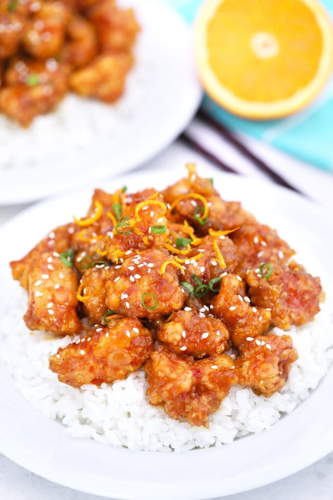 Orange chicken with sesame seeds garnished with sesame seeds over a bowl of white rice. 