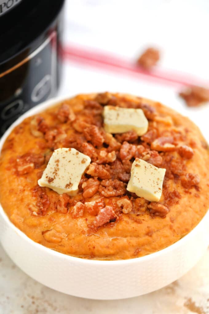 Mashed sweet potatoes garnished with pecans, butter and cinnamon on a white plate