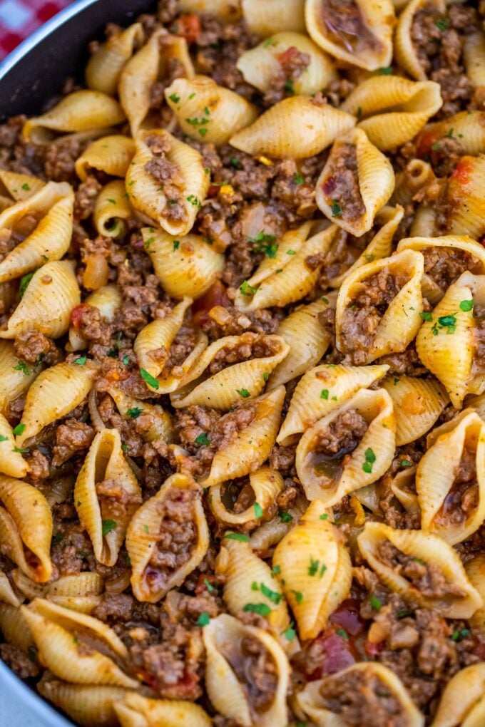 taco pasta with pasta shells and ground beef garnished with chopped parsley in a skillet.