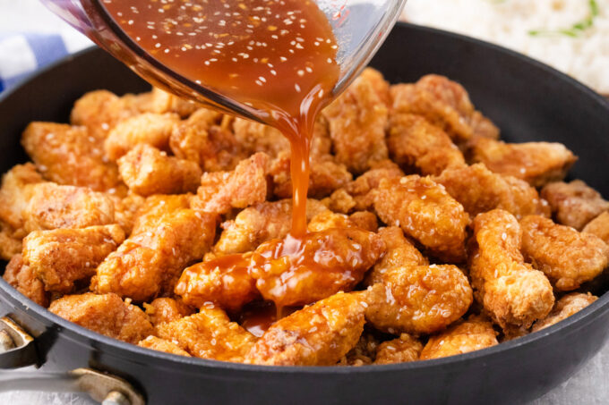 Adding honey sesame oil to fried chicken pieces.