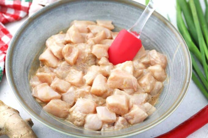 Velveting chicken pieces in a bowl of cornstarch mixture.