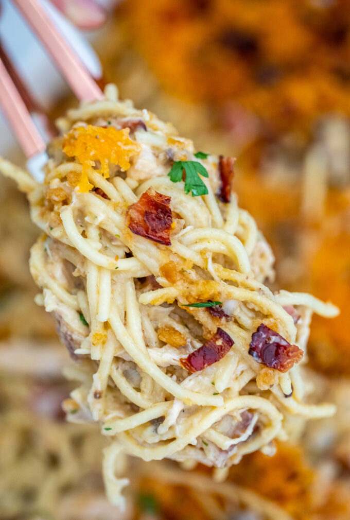 kitchen tongs holding crack chicken spaghetti casserole with bacon.