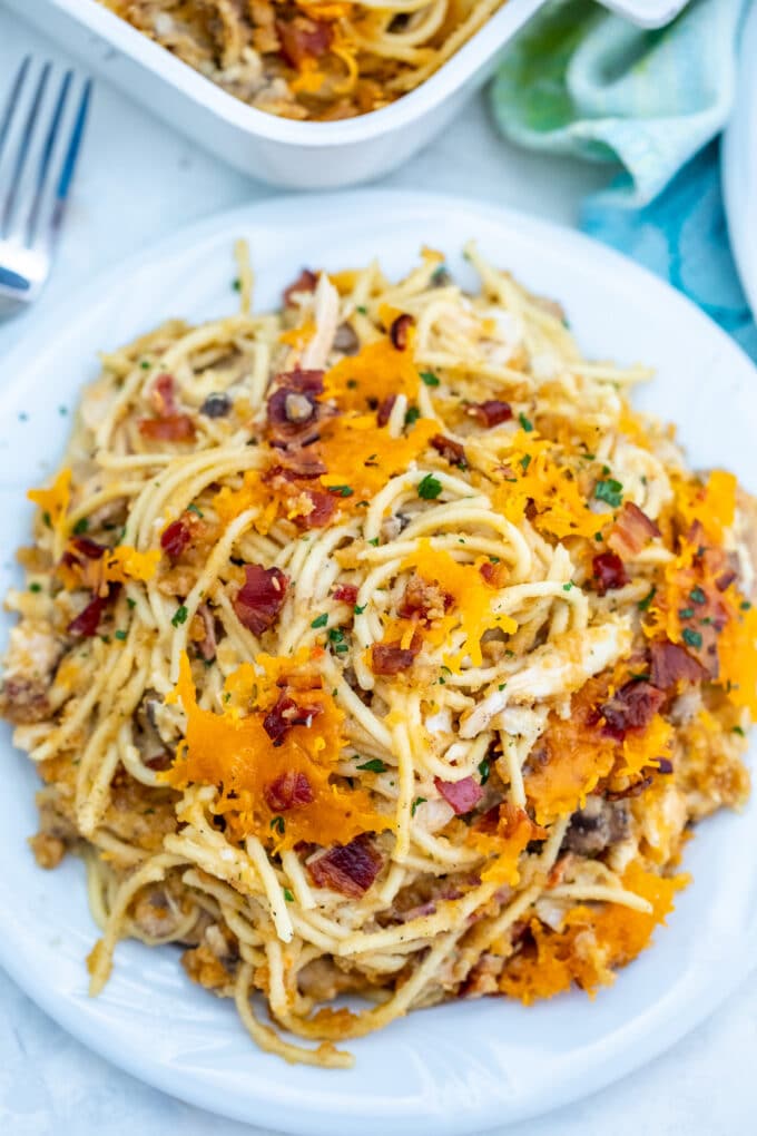 homemade chicken spaghetti casserole on a plate, topped with cheddar cheese and bacon