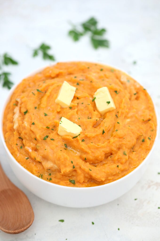 homemade creamy mashed sweet potatoes in a white bowl topped with butter pieces