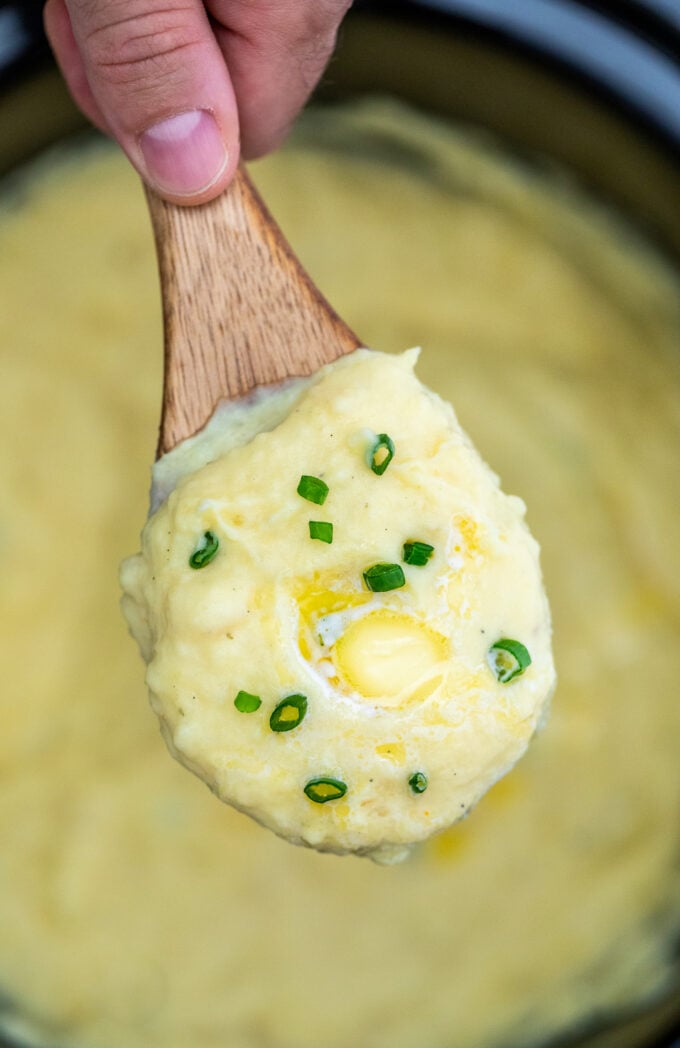A spoonful of creamy mashed potatoes topped with chopped green onion and butter