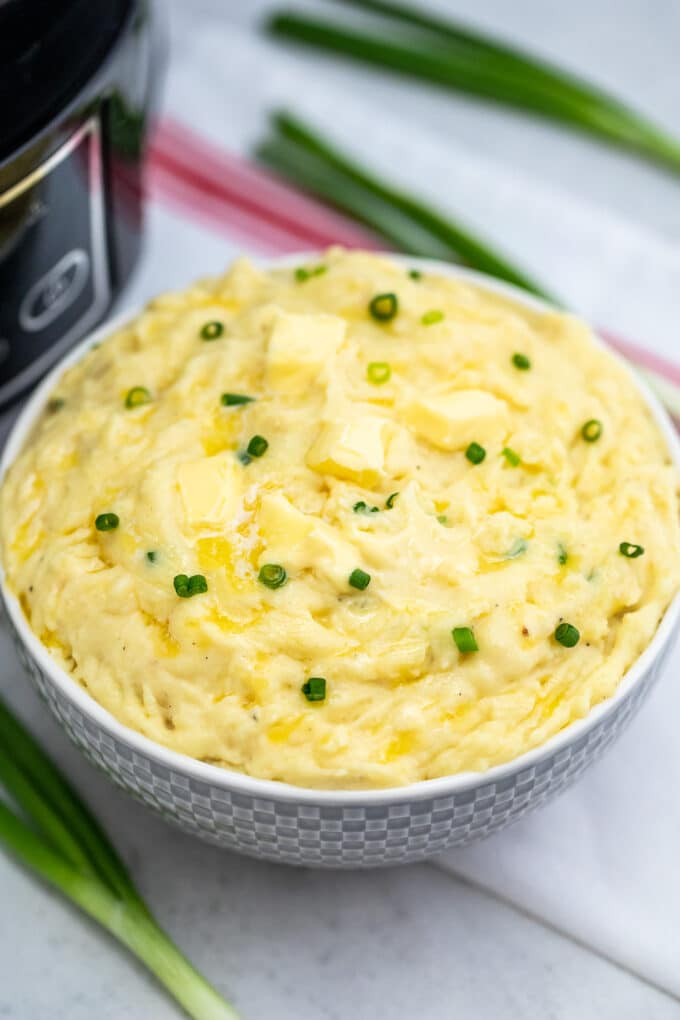 Slow cooker mashed potatoes topped with butter and green onions in a white bowl