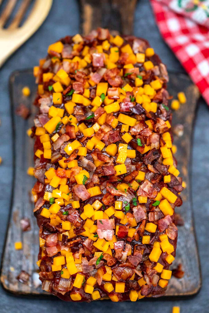 Bacon cheeseburger meatloaf topped with bacon and cheese on a wooden board.