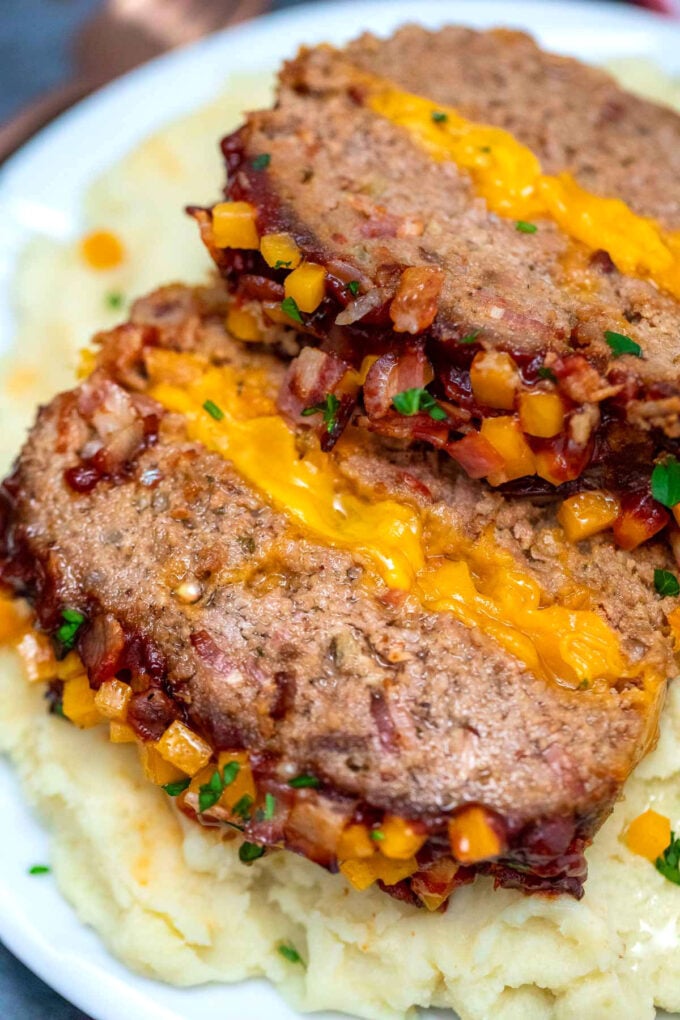 Homemade bacon cheeseburger meatloaf over mashed potatoes on a white plate.