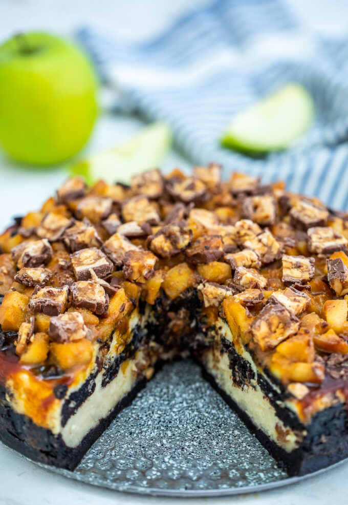 Apple Snickers Cheesecake is not your ordinary dessert! It has your favorite chocolate bar and fruit rolled into one unique and unforgettable cheesecake! #cheesecake #snickers #appledesserts #sweetandsavorymeals #halloweenrecipes