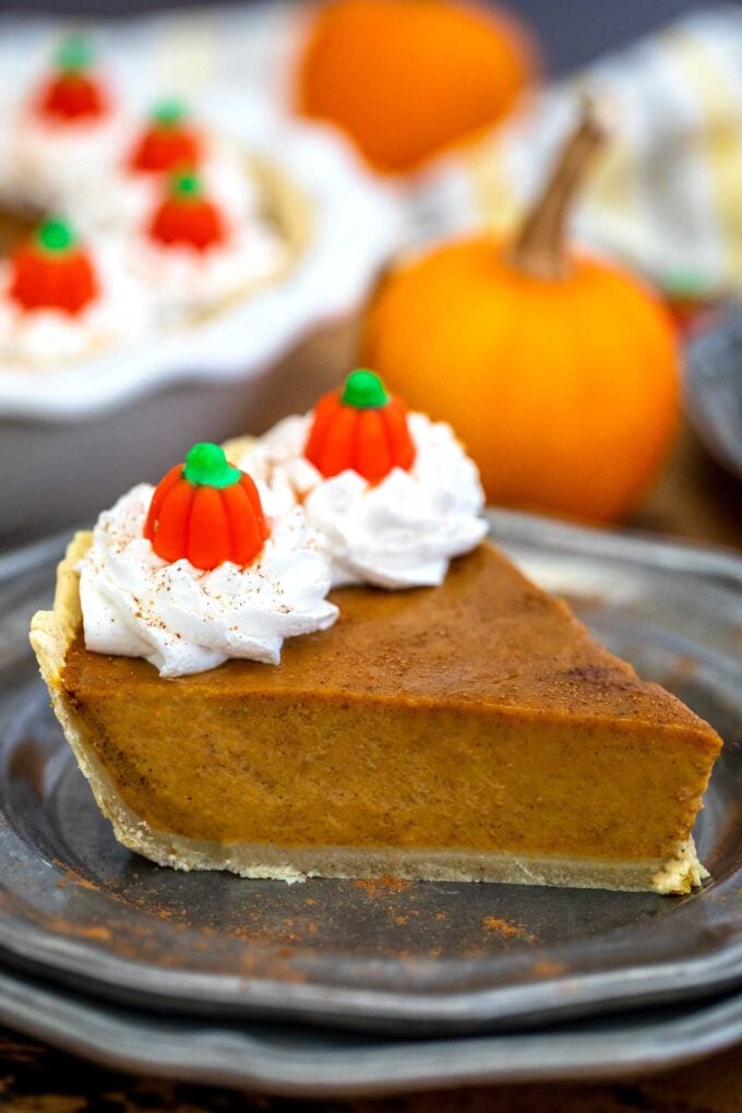 A slice of homemade pumpkin pie on a silver plate topped with whipped cream
