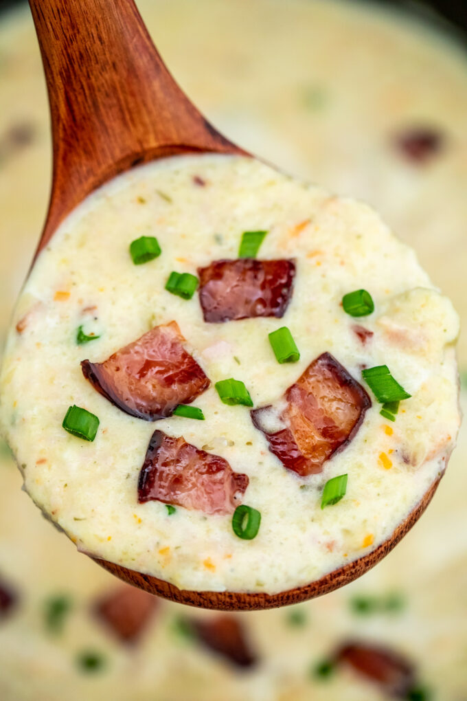 A spoonful of ham and potato soup garnished with bacon and chopped green onion.