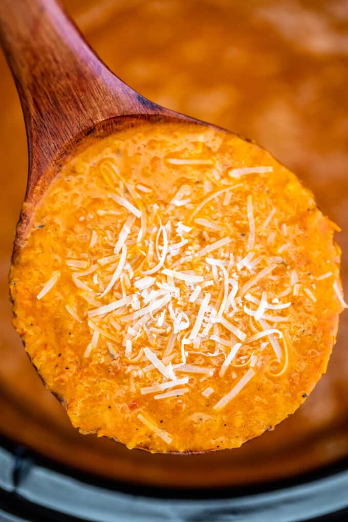 Tomato soup garnished with shredded cheese on a wooden spoon