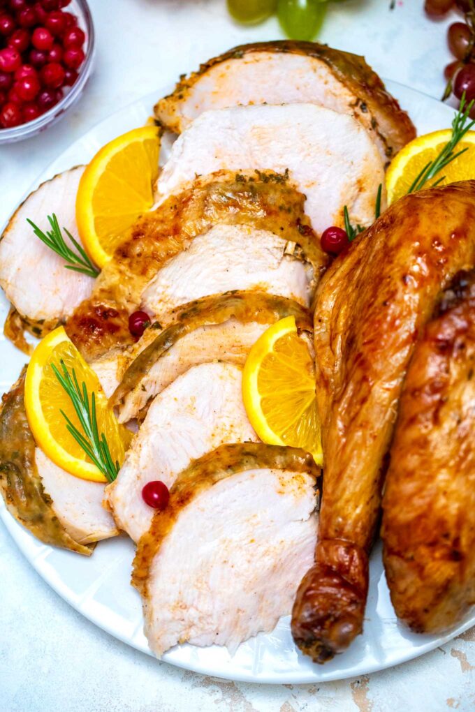 slices of oven roasted turkey and a turkey thigh on a serving plate with rosemary and orange slices