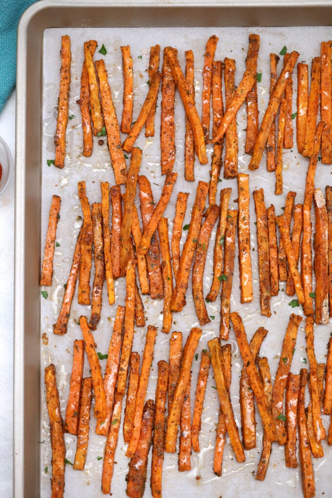 Crispy roasted sweet potato wedges on a baking sheet and topped with shredded cheese.