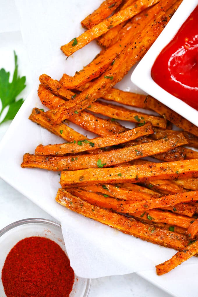 Crispy oven roasted sweet potato fries and ketchup on a white plate. 