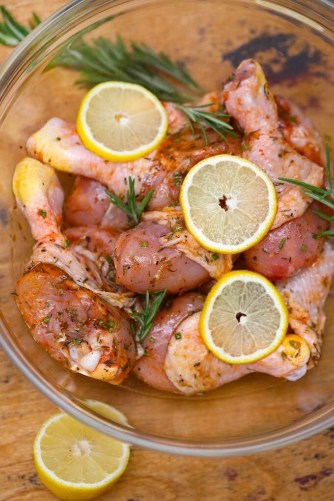 Marinated chicken legs with lemon and rosemary in a large glass bowl