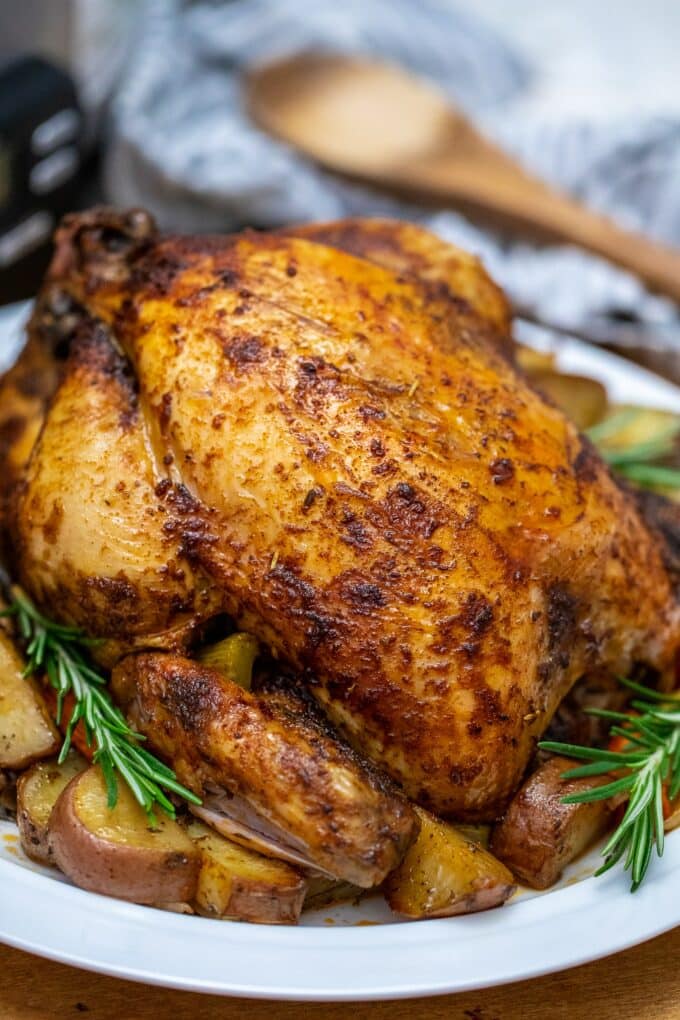 Slow cooker whole chicken with rosemary over potatoes on a white plate