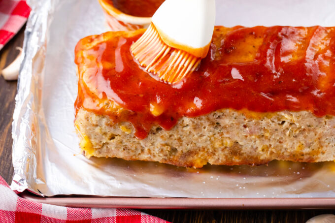 Brushing cheesy turkey meatloaf with Pepper Jack cheese with tangy meatloaf glaze.