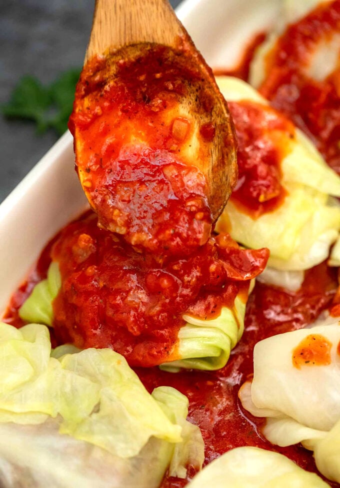 adding tomato sauce on top of a stuffed cabbage roll in a baking dish