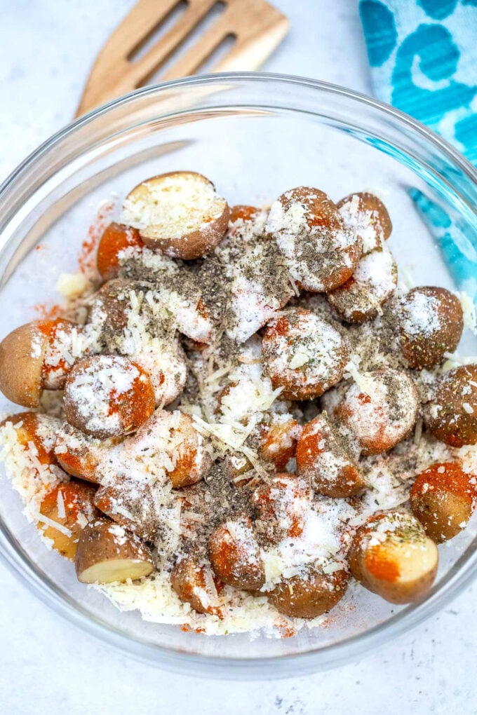 Red baby potatoes with shredded cheese and seasoning in a large glass bowl