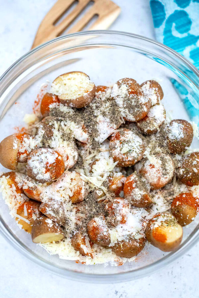 Baby potatoes with shredded cheese and seasoning in a large glass bowl to make air fryer potatoes