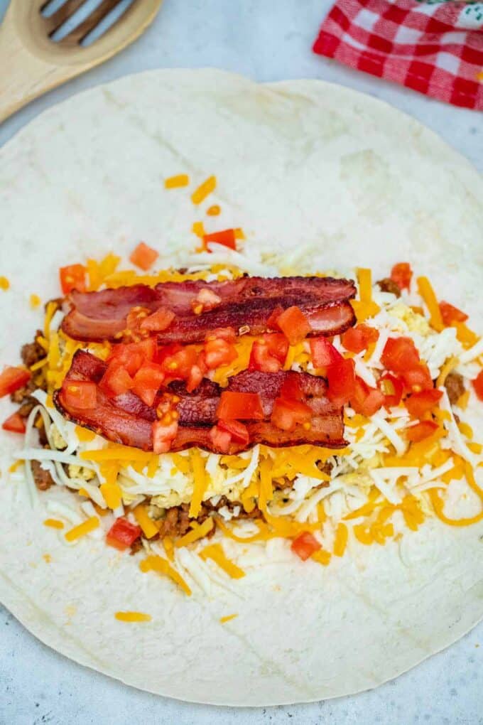 assembling sausage egg and cheese breakfast burrito on a flour tortilla