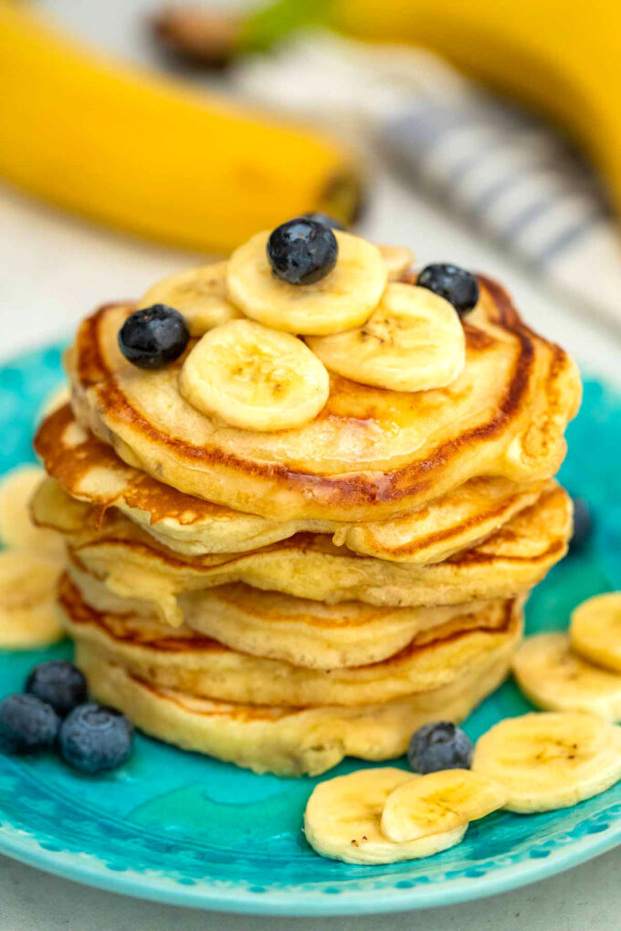 photo of stacked banana pancakes topped with blueberries and bananas
