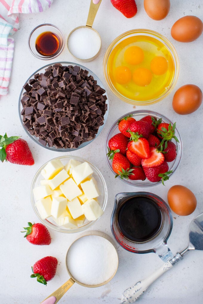 Overhead shot of chocolate flourless cake ingredients in bowls on a white surface.