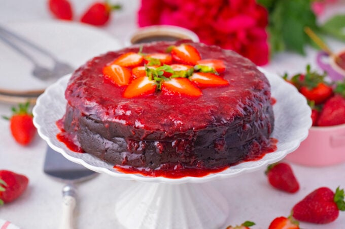 Homemade chocolate flourless cake with berry sauce on a cake stand.
