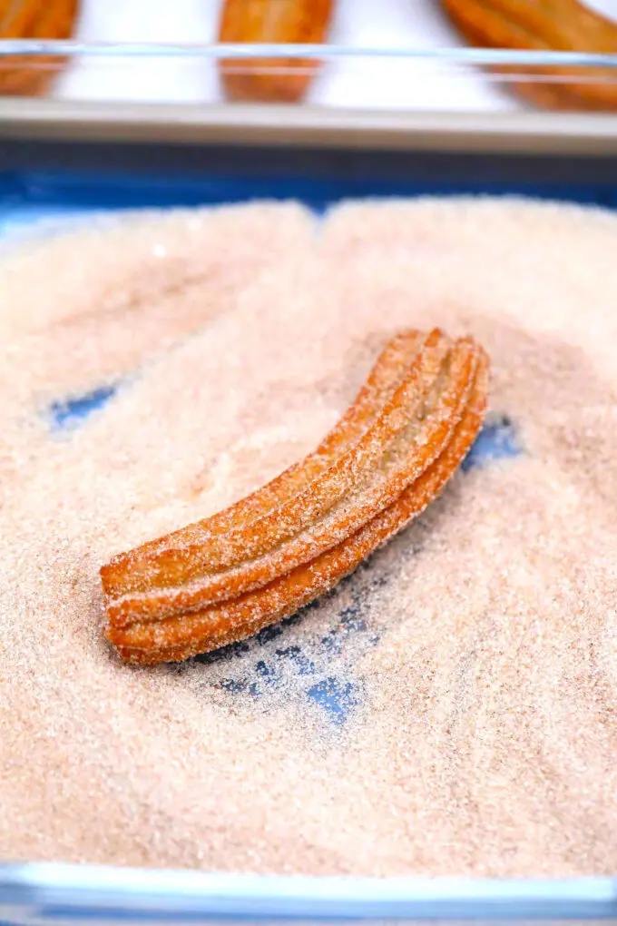 coating a churro in cinnamon sugar