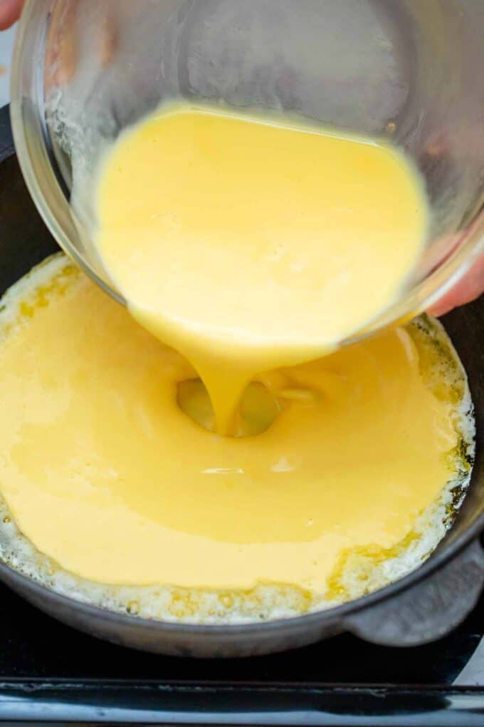 pouring beaten eggs in a cast iron skillet