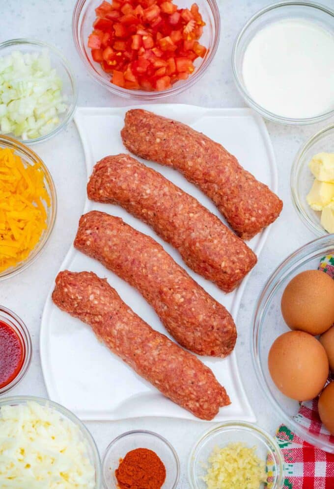 sausage egg and cheese breakfast burrito ingredients in bowls, arranged on a white surface.