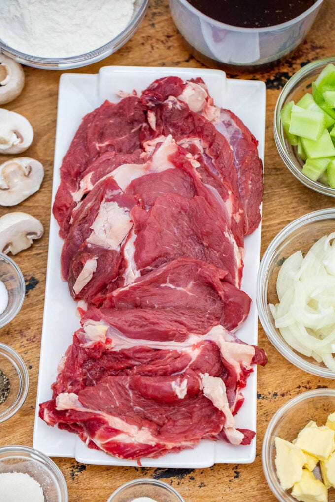 Overhead shot of slow cooker Swiss steak ingredients arranged on a wooden table.