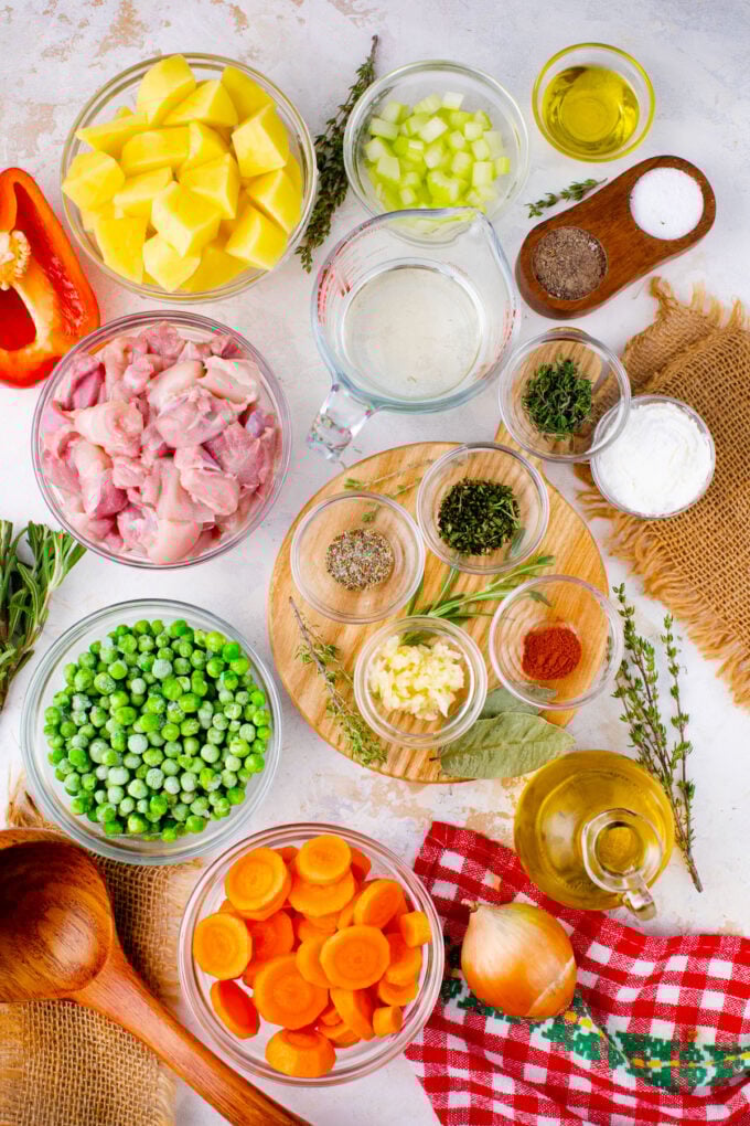Overhead shot of slow cooker chicken stew ingredients in bowls on a white surface.