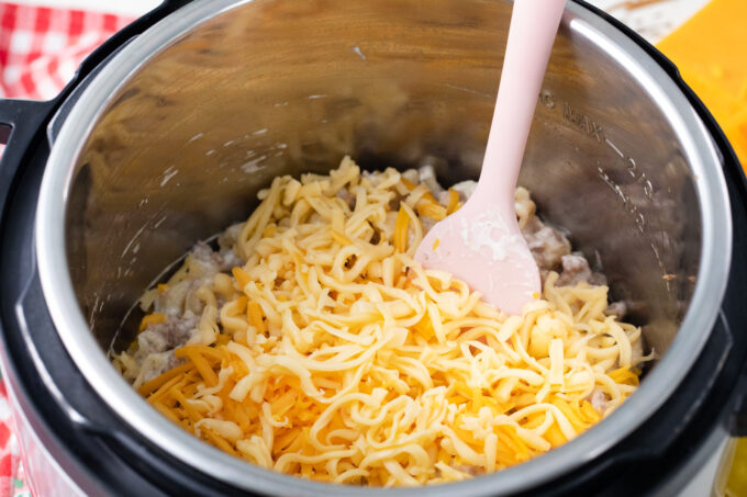 Adding shredded cheese to Instant Pot cheeseburger macaroni.