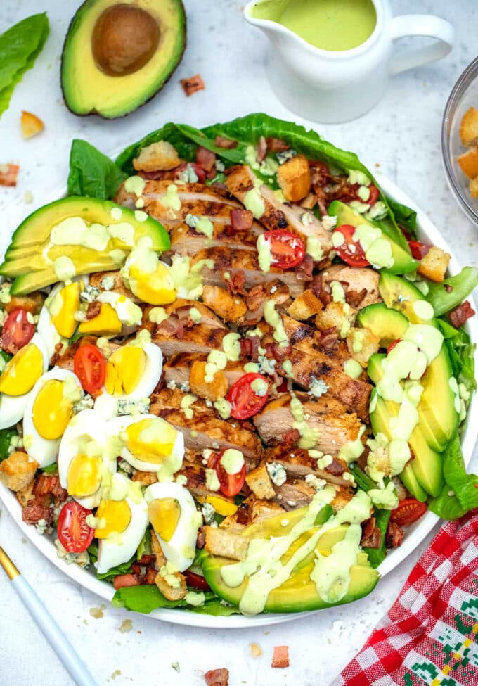 Homemade salad made with chicken, lettuce, eggs, and avocado on a white plate.