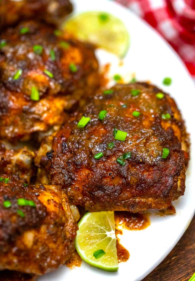 jerk chicken thighs on a plate with sliced limes