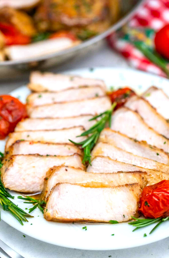 Picture of sliced juicy pork chops with roasted tomatoes and rosemary.