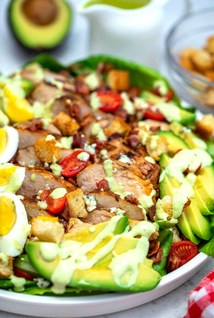 Cobb salad with eggs chicken and homemade dressing on a white plate.