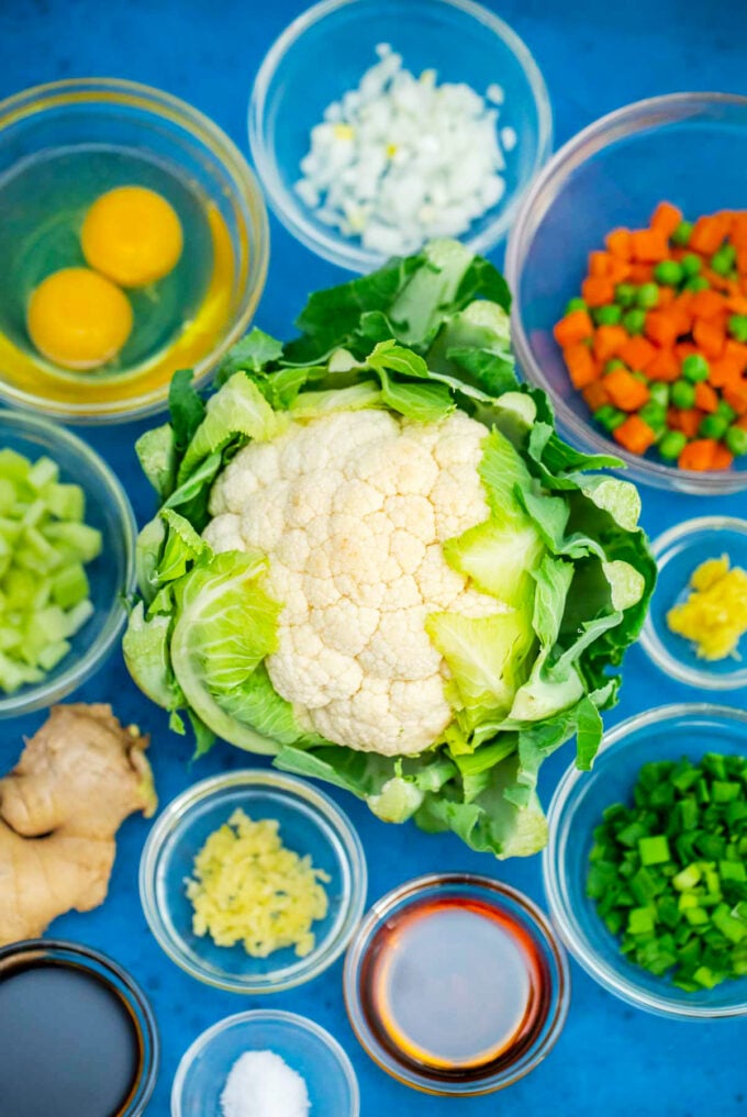 Overhead shot of low carb cauliflower rice ingredients in bowls on a blue surface.