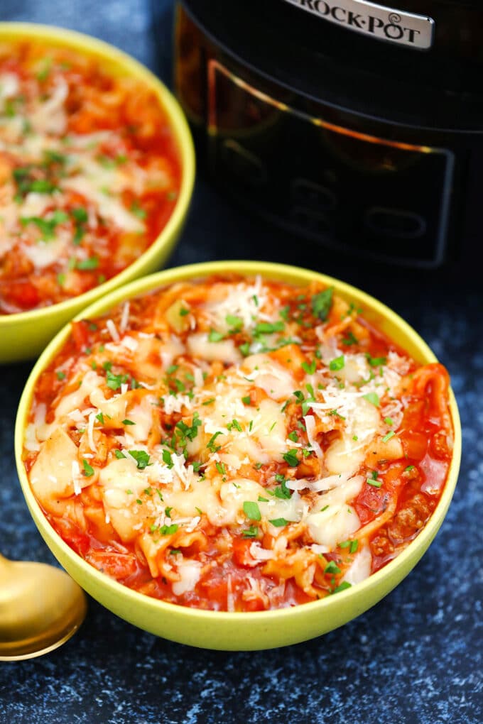 A bowl of homemade lasagna soup garnished with shredded cheese and chopped parsley.